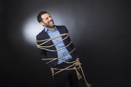 Uomo con giacca e camicia legato da un fune è disperato perché non può muoversi liberamente - sfondo nero